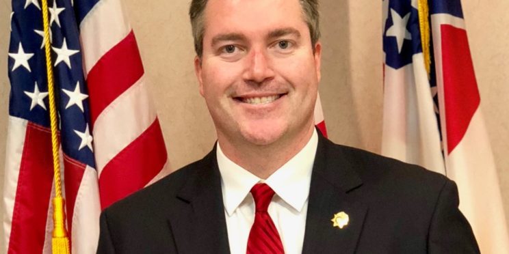 Josephy Willoughby poses in a suit in front of the American flag.